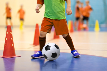 Football futsal training for children. Soccer training dribbling cone drill. Indoor soccer young player with a soccer ball in a sports hall. Player in orange uniform. Sport background.