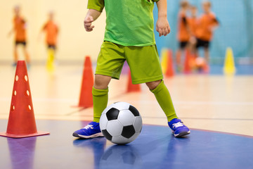 Football futsal training for children. Soccer training dribbling cone drill. Indoor soccer young player with a soccer ball in a sports hall. Player in yellow uniform. Sport background.
