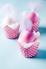 a group of three pink eggs decorated with feathers in paper stands. Easter background, vertical photo