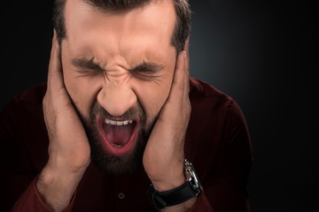portrait of screaming man covering ears isolated on black