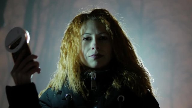 4k Red hair strange woman with lamp standing at dark winter park with creepy light  close-up