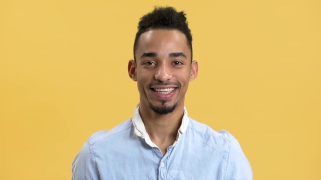 Portrait of pleased man with arabic appearance in shirt looking on camera and smiling, isolated over yellow background. Concept of emotions