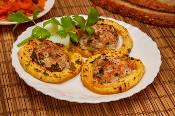 Baked slices of zucchini stuffed with minced meat from turkey, with bread and greens of celery, on a white plate, on a napkin made of bamboo. Closeup