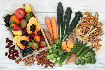 Health food high in fibre with whole wheat pasta, nuts, fruit and vegetables with super foods high in antioxidants, omega 3 fatty acids, anthocyanins and vitamins. Rustic background, top view.