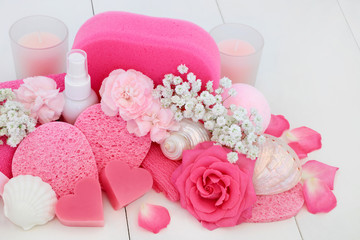 Spa and bathroom beauty treatment accessories with pink rose and carnation flowers, heart shaped soaps, body lotion, bath bomb, sponges, wash cloth, ex foliating scrub with decorative seashells.