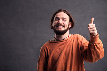 Portrait of male blogger, bearded happy man showing thumb up in the gray background