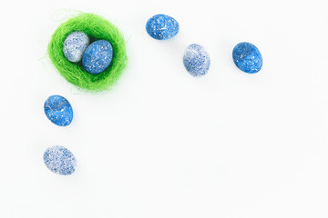 Frame made of blue speckled Easter eggs with bright nest on white background. Flat lay. Top view
