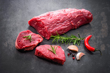 Whole piece of tenderloin with steaks and spices ready to cook on dark background