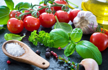 Ripe tomatoes with fresh basil, garlic and other herbs with water drops on slate plate