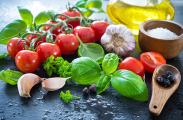 Ripe tomatoes with fresh basil, garlic and other herbs with water drops on slate plate