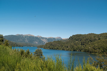 Lake landscape surrounded by mountains and vegetation, with a blue sky