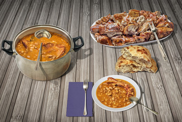 Beans Baked With Smoked Pork Ribs Served With Plateful Of Spit Roasted Piglet Meat Slices And Domestic Leavened Flatbread On Rustic Slatted Wooden Place Mat