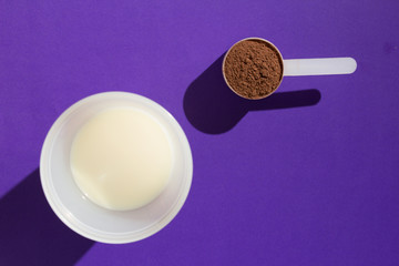 Obraz na płótnie Canvas Whey Protein. Minimalism concept and hard light. Scoop with chocolate powder and glass of milk on violet background.