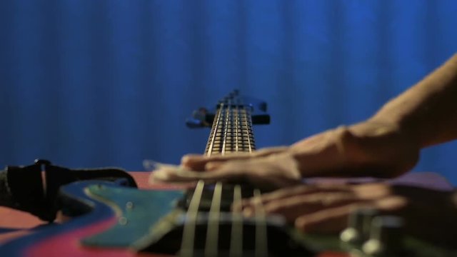 In workshop craftsman carefully wipes strings of old bass guitar