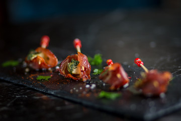 parma ham and cheese skewers with olive oil on black plate with salt and peppercorns