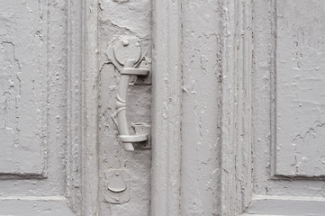 Close-up keyholes with curtains and a handle on the gray many times painted cracked double-barreled wooden vintage door of the last century with a post slit.