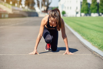 Ready to go! Female athlete on the starting line of a stadium track, preparing for a run. Fitness girl is preparing to run from a low start. Healthy lifestyle.