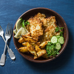 Fried fish and garlic baked potatoes on a blue background, top view. Fish and chips