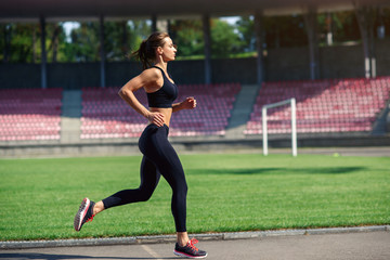 Young fitness woman running on a stadium track. Athlete girl doing exercises on the training at stadium. Healthy active lifestyle.