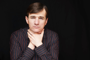 A handsome man in a black shirt holds his neck and сhoke himself on the black background because he has stress