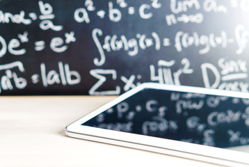 Modern education and e learning concept. Tablet in front of a blackboard full of writing at school. Smart mobile device and chalkboard in classroom. Learning with technology. Digital exam.