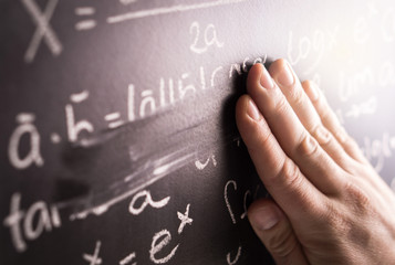 Making mistakes and wrong answer concept. Hand wiping math formula off blackboard in classroom at...