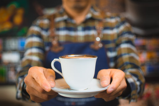 Close up hand of barista holding classic white coffee cup to customer. Image selective focus.