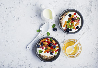 Yogurt, milk porridge, granola for breakfast with different berries, nuts and fruits: kiwi, pomegranate, dried apricots, blueberries, almonds and honey. Portionally. Top view Food concept.