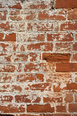 An old weathered, damaged, formerly painted, badly repaired red brick wall full frame background