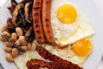 Traditional full English breakfast with fried eggs, sausages, beans, mushroomsand bacon on wooden background