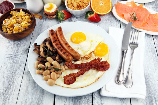 Traditional full English breakfast with fried eggs, sausages, beans, mushroomsand bacon on wooden background