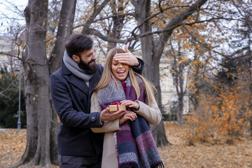 Young beautiful couple in park, he give to her present and she is looking so surprise