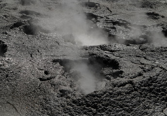 Steaming black magma surface with rising geothermal vapor trails. Little geyser with steam.