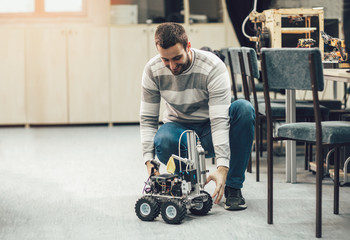 Young student of robotics preparing car robot for testing in workshop