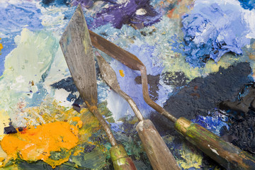 Well used artists palette knives on a multi-coloured paint palette