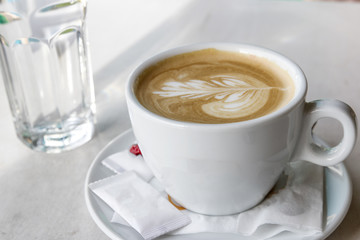 Mug with cappuccino with small bags of sugar and glass of water at the table
