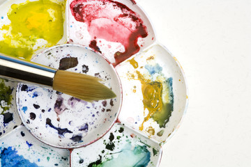 Artists flower shaped style watercolour palette and brush on a white textured paper background with copy space