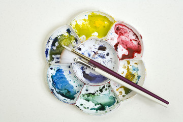 Artists flower shaped style watercolour palette and brushes  on a white textured paper background...