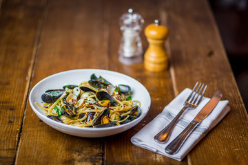 spaghetti vongole italian seafood pasta dish on white plate  on wooden table with fork and knife and salt and pepper