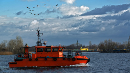 The orange boat is moving along the pond