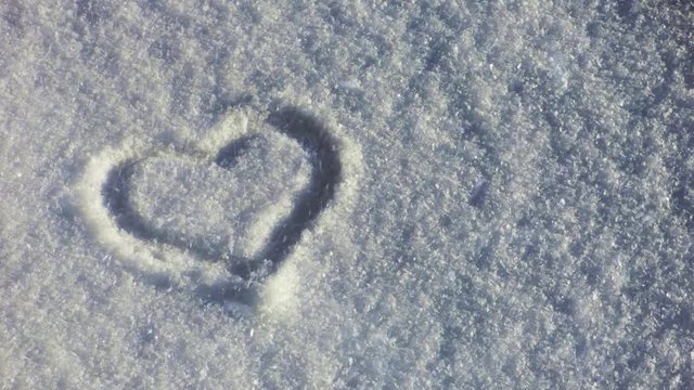 Heart symbol on the snow, lot of snowflakes flying on the wind. Romantic sign silhouette on winter ground. Valentines day natural background.