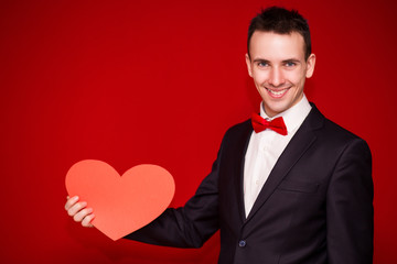 Stylish man in suit hold white paper heart on red backgroundt. Valentines day composition