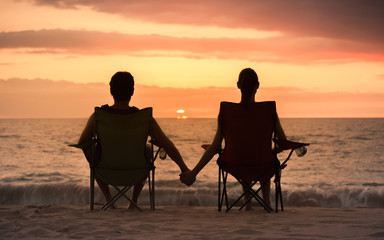 Fototapeta na wymiar Couple relaxing on the beach watching the sunset holding hands. 