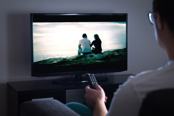 Man watching tv or streaming movie or series with smart tv at home. Film or show on television screen. Person holding the remote control or switching channel. Turning on or off tv.