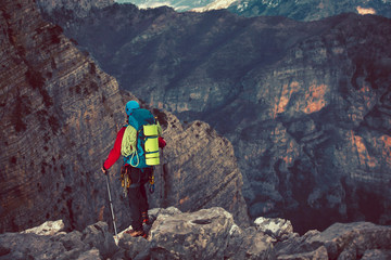 Young mountaineer standing with backpack on top of a mountain and enjoying the view