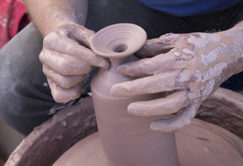 Potters hands covered in clay forming a pot on a wheel