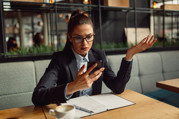 Portrait of cute young confused business woman using smartphone and looking at the screen.