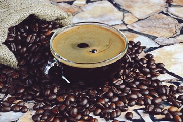 Cup of aromatic espresso with steam and coffee beans background. Cup of coffee isolated