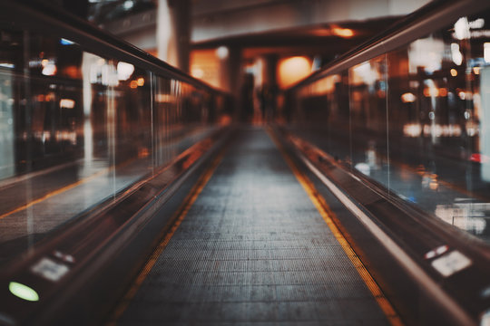 Shooting with shallow depth of field of moving walkway in modern airport terminal waiting hall; travelator trough departure area of railway station depot with multiple bokeh shapes around