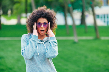 a beautiful girl in lilac glasses, with an afro hairdo, smiling and laughing, in a park on a...